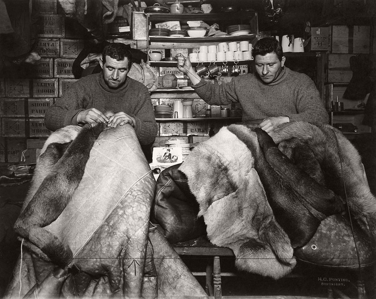Expedition members repair reindeer-fur sleeping bags inside the Terra Nova hut on May 16, 1911.  For the South Pole journey, the men wore warm, reindeer-fur boots called finneskos, oversize reindeer-fur mitts, and goggles to prevent snow-blindness.