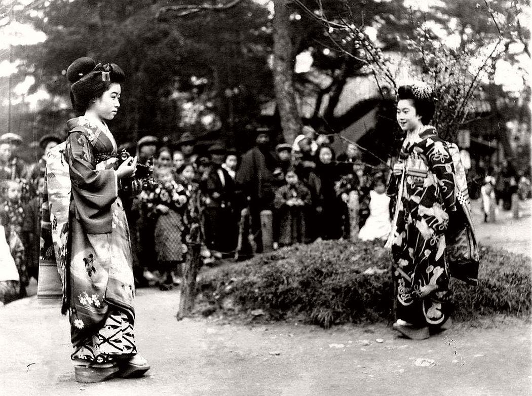 One Maiko taking a photograph of another withe an early Kodak folding camera, ca. 1920s