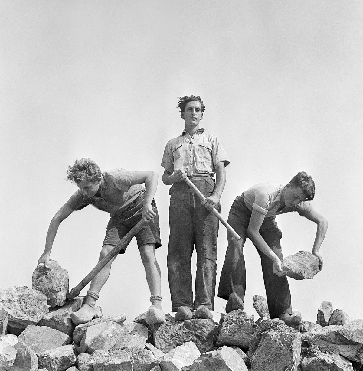 Roman Vishniac, [Ernst Kaufmann, center, and unidentified Zionist youth, wearing clogs while learning construction techniques in a quarry, Werkdorp Nieuwesluis, Wieringermeer, The Netherlands], 1939. Ink-jet print. © Mara Vishniac Kohn, courtesy International Center of Photography.