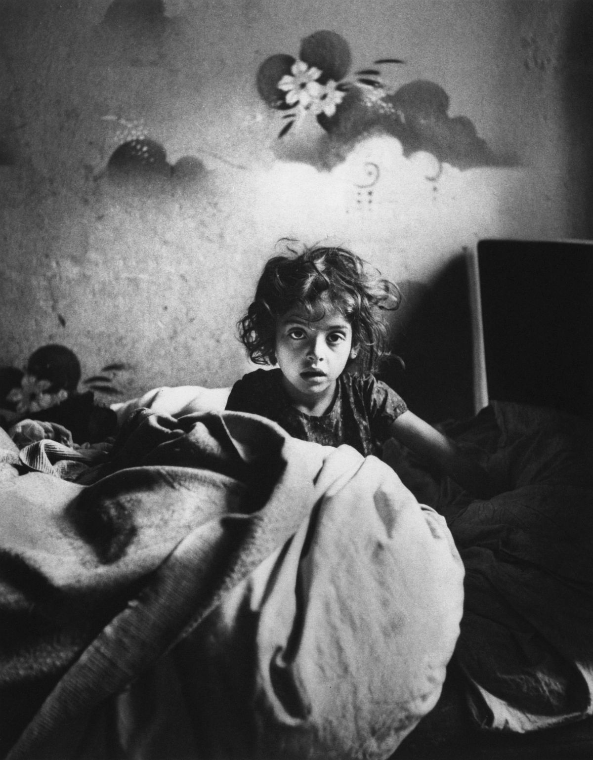 Roman Vishniac, [Sara, sitting in bed in a basement dwelling, with stenciled flowers above her head, Warsaw], cs. 1935–37. Platinum print. © Mara Vishniac Kohn, courtesy International Center of Photography. 