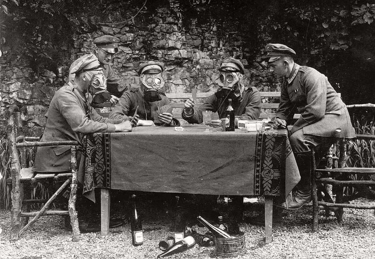   German NCOs from Infanterie-Regiment No. 358 pose for the photographer as if they were drinking wine, feasting on gherkins and playing cards while wearing gas masks. # Brett Butterworth
