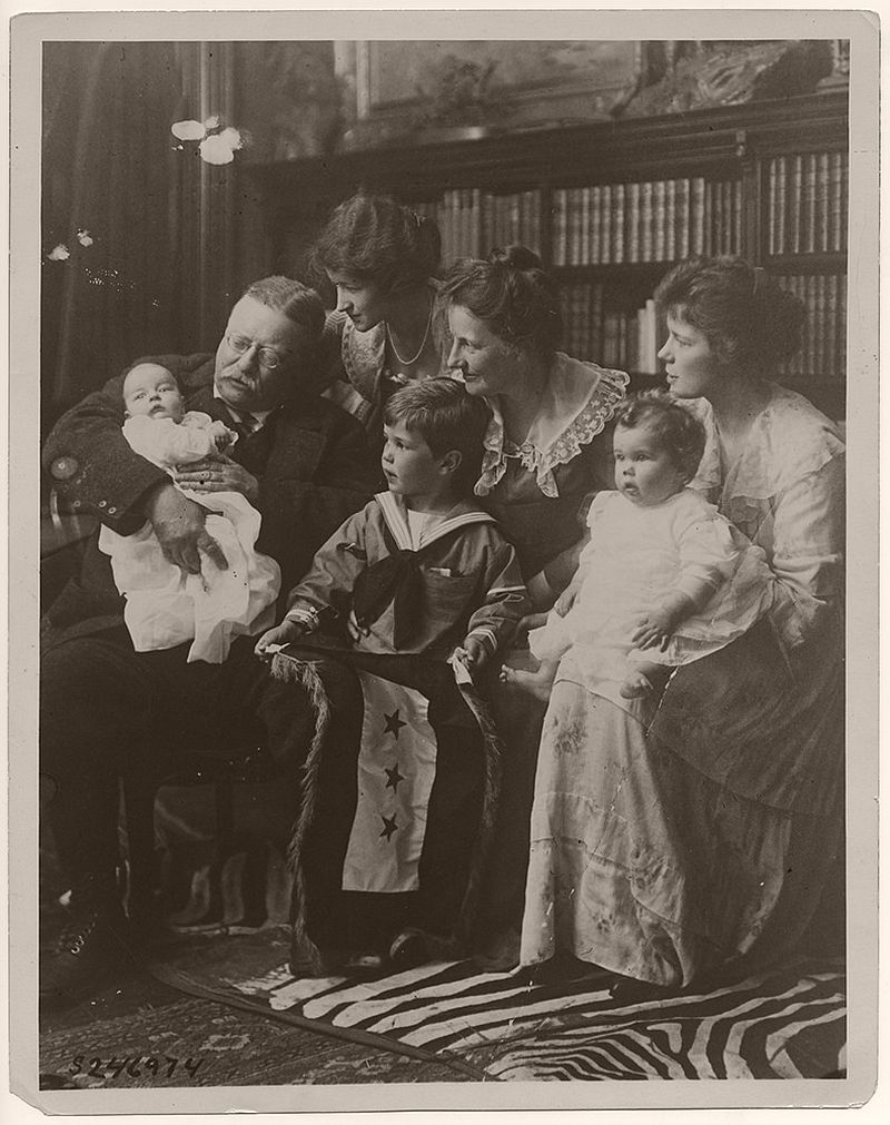 Seated, left to right, are Archibald Bulloch Roosevelt, Jr., Theodore Roosevelt, Grace Stackpole Lockwood Roosevelt, Richard Derby, Jr., Edith Kermit Carow Roosevelt, Edith Roosevelt Derby Williams, and Ethel Carow Roosevelt Derby. Richard Derby Jr. is holding a service flag with three stars. The stars symbolize three of Roosevelt's sons, Quentin, Archie, and Theodore Jr., who served the United States in battle.