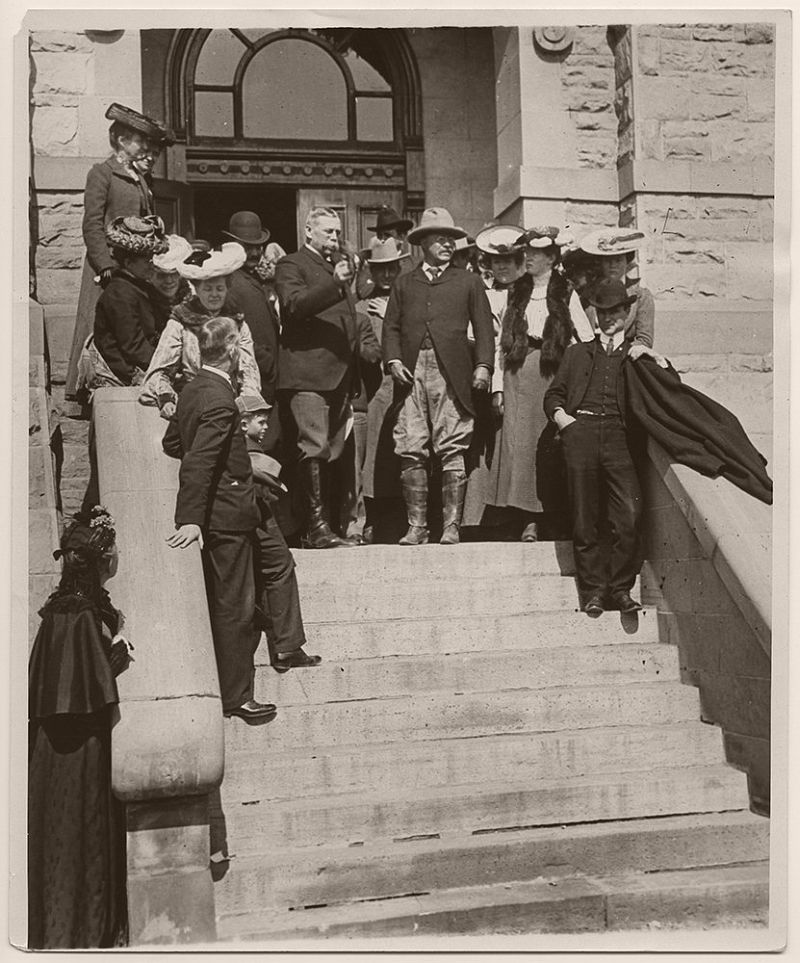 President Theodore Roosevelt receiving a pair of spurs from Francis Warren, United States Senator for Wyoming at the Cheyenne Public Building, which served as courthouse for the District of Wyoming. Presidential Secretary, William Loeb, Jr., is seen immediately behind Senator Warren. President Roosevelt was also given a horse and saddle while in Cheyenne. June 1, 1903.