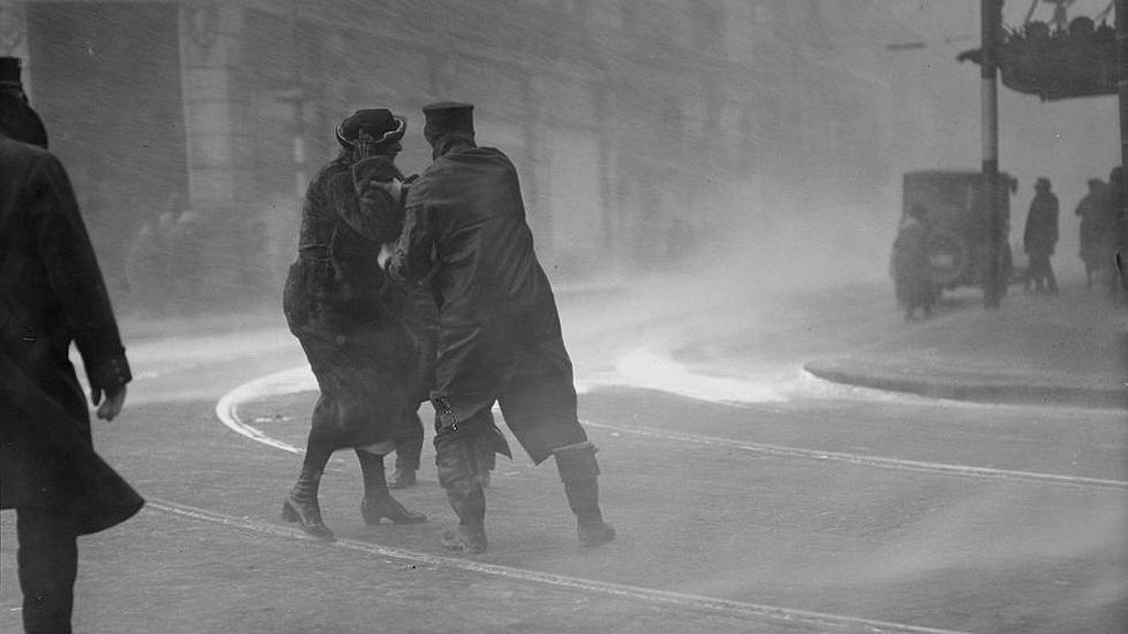 Circa February 1920. Police officer helps woman through blinding snow during a blizzard in Boston.