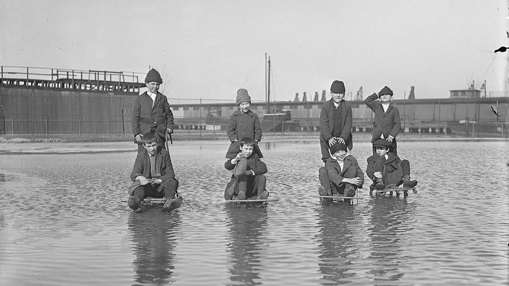 Circa 1921. Kids on sleds plough through water to enjoy ice hidden below.