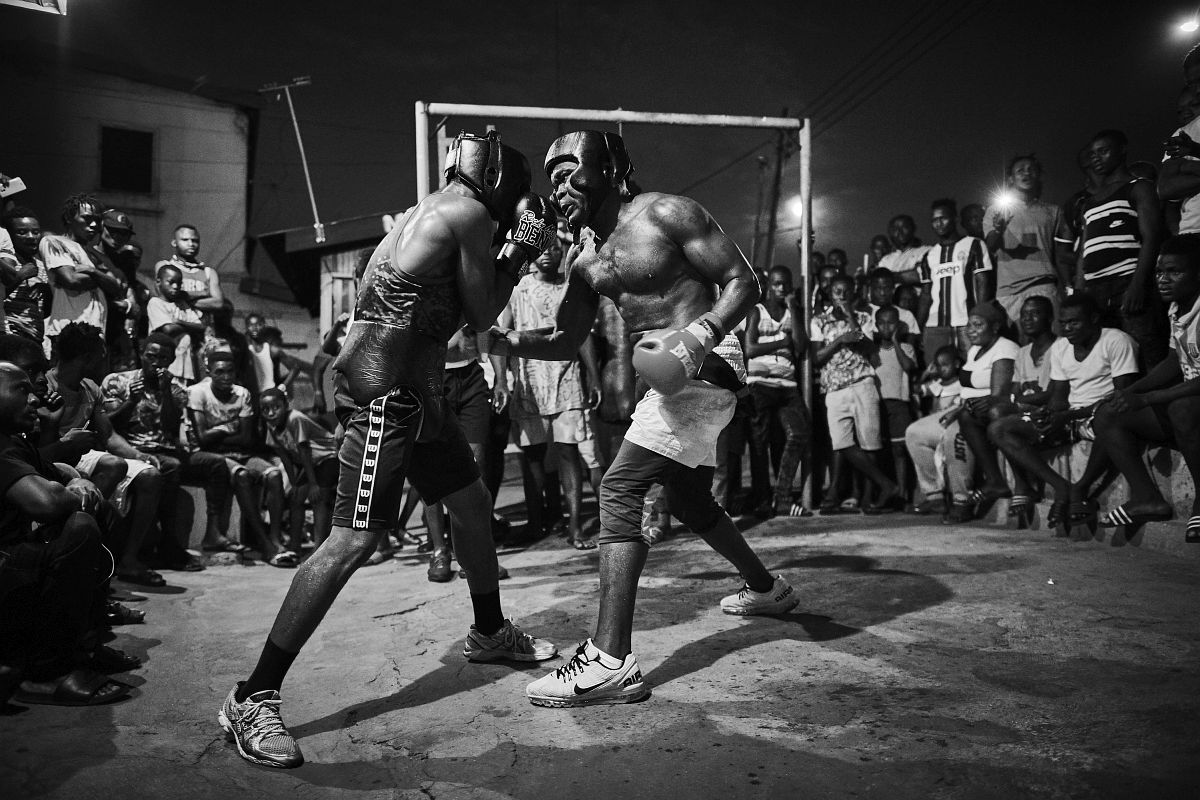 From Right - Boxer Braimah Kamoko, aka "Bukom Banku" sparring with George Ashie aka "Red Tiger" at "Wadada Boxing Gym" in preparation for Kamoko´s fight with Bastie Samir. Accra, Ghana, October 4th, 2017.<br /> Crowds of cheering fans encircle the two boxers to cheer on their hero "Bukom Banku". Many of these fans have run long distances to support the boxers in their training session.