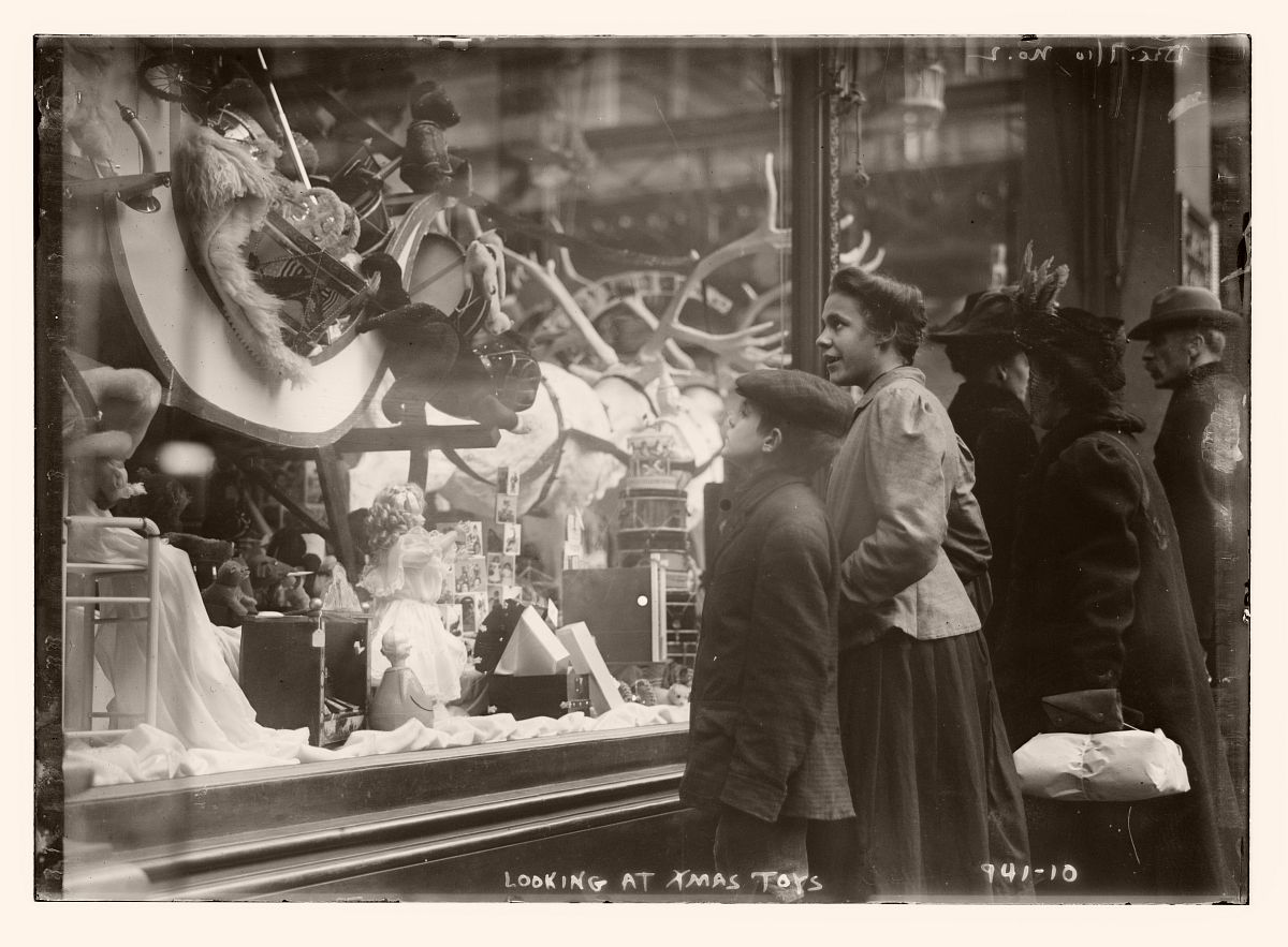 Woman and young boy looking at window of shop where Xmas toys are displayed