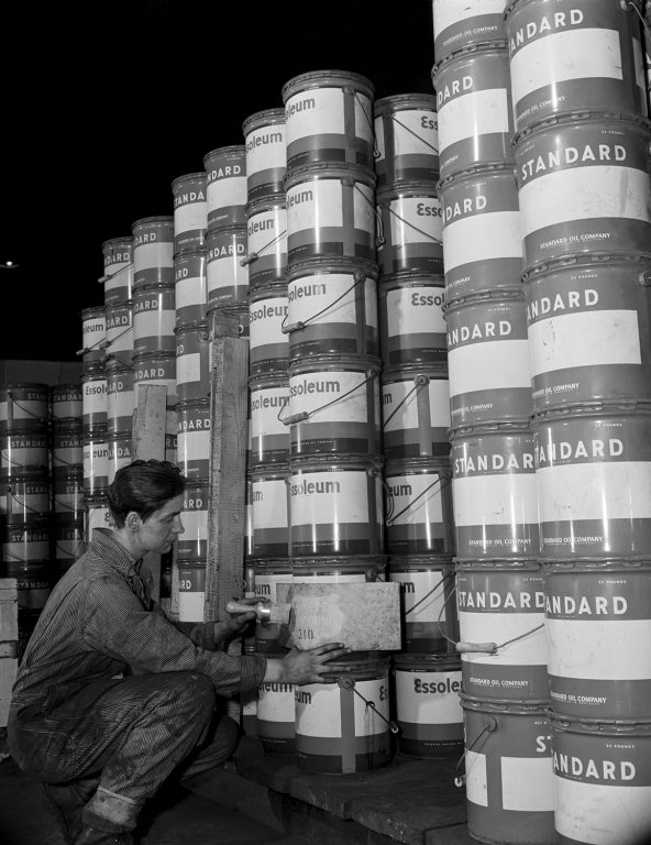 Gordon Parks, After lubricants are packed and containers placed in large rows for shipment, a man with the properly cut stencil markseach can or drum with the name and number of the grease it contains., 1944, courtesy of the Gordon Parks Foundation